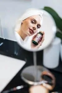 Djevojka drzi bocicu Hug Your Life Beauty Harmony - Hair, Skin & Nails dodatka prehrani u kupaonici pred ogledalom