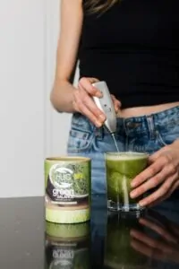 Djevojka priprema zdravi napitak s Hug Your Life Green Balance dodatkom prehrani u kuhinji