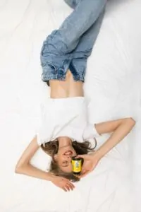 Djevojka lezi na krevetu opustena i drzi bocicu Hug Your Life Magnezij Chelate 5 Kompleks dodatka prehrani