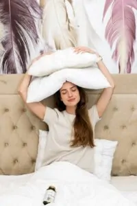 Djevojka lezi u krevetu s jastucima iznad glave s bocicom Hug Your Life Natural Sleep On PLUS dodatka prehrani