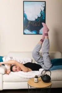 Djevojka lezi opusteno na kaucu s nogama u zraku s bocicom Hug Your Life Natural Stress off dodatka prehrani na stolicu pored