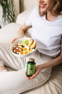 Djevojka drzi zdjelu sa zdravom hranom i bocicu Hug Your Life Nature's MultiVitamins dodatka prehrani
