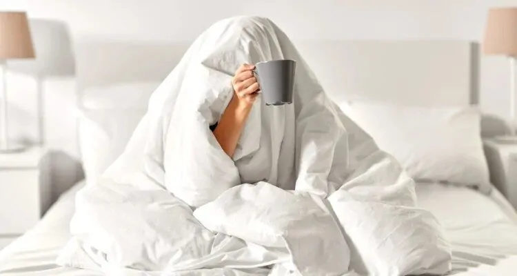 Djevojka pokrivena s poplunom u krevetu, drzi salicu