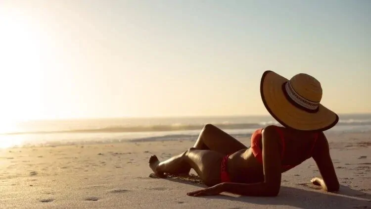 Mlada žena leži na pijesku i nosi šešir, a zaštitila je kožu astaksantinom