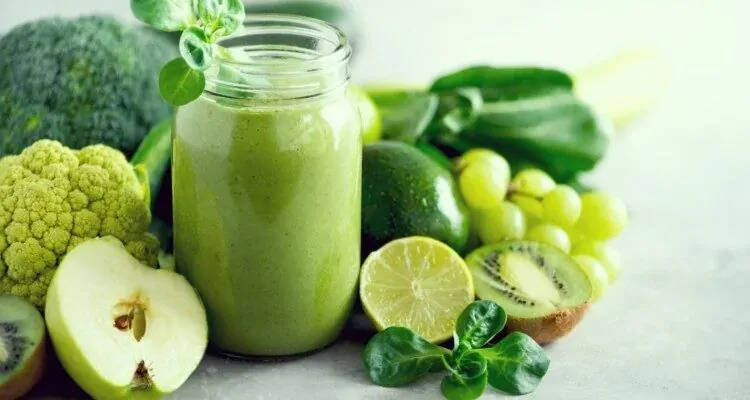 Zeleni smoothie u staklenoj casi na stolu pored kiwia, limete, zelene jabuke i ostalih zelenih namirnica